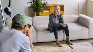 Maria Höfl-Riesch sitzt auf der Couch in einem Studio und schaut zum Fotografen in der linken unteren Bildecke. Im Hintergrund sieht man Studiobeleuchtung und Stative.