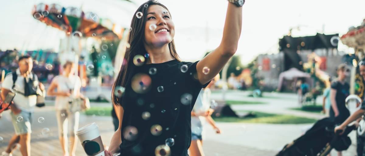 Lächelnde Frau zu Besuch in einem Vergnügungspark mit fliegenden Seifenblasen vor ihr