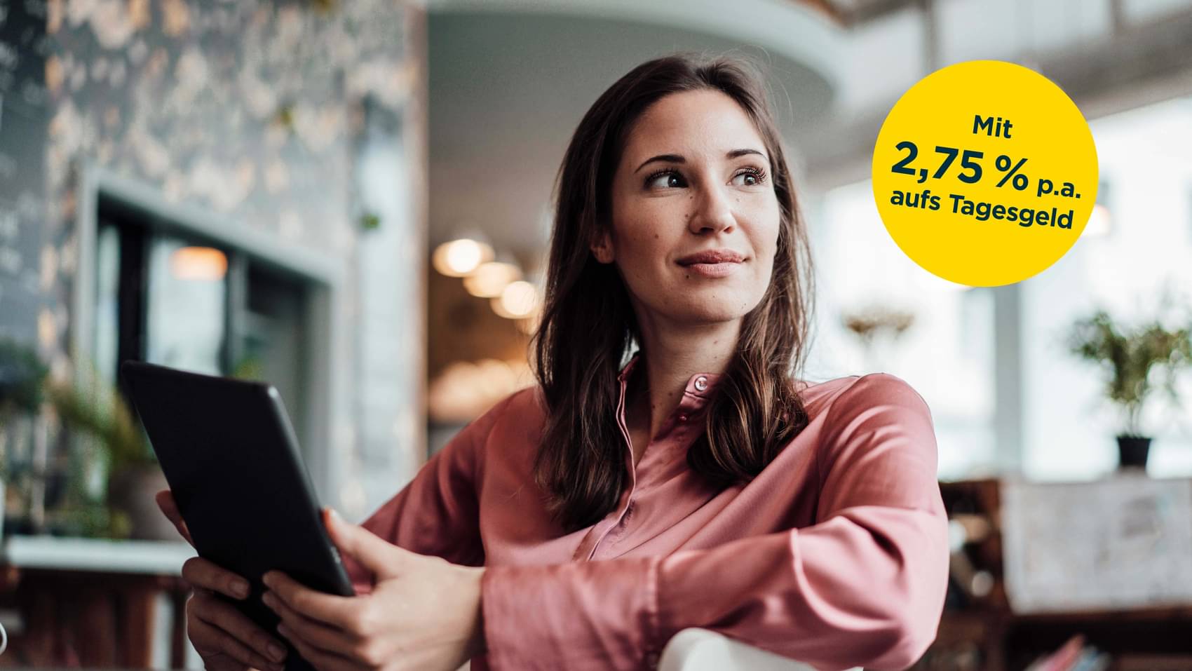 Frau sitzt entspannt auf einem Stuhl mit einem Tablet in der Hand, 2,75% p.a. aufs Tagesgeld