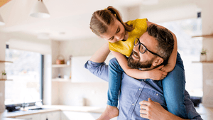 Ein Vater trägt sein Kind in der Wohnung auf den Schultern.
