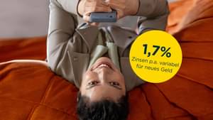Eine Frau liegt rücklings auf einem Futon und schaut auf ihr Smartphone: 1,7 Prozent Zinsen p.a. für neues Geld (Tagesgeldkonto)