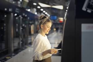 Eine Frau steht am Bankautomat und steckt ihre Bankkarte ein.