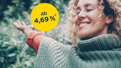 Frau steht glücklich im Wald und breitet die Arme aus: Klimakredit ab 4,69% p.a.*