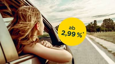 Junge Frau mit blonden Haaren sitzt auf der Beifahrerseite eines Autos und lehnt sich mit Arm und Kopf zum offenen Fenster raus: Autokredit ab 2,99% p.a.*