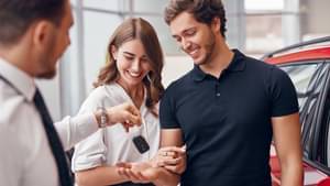Ein Verkäufer gibt einem jungen Paar die Schlüssel zu ihrem neuen Auto.