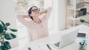 Junge Frau, die an ihrem Schreitisch sitzt und sich entspannt in ihrem Stuhl zurücklehnt