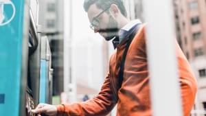 Mann steht in einer Großstadt vor einem Automaten