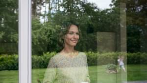 Frau steht mit ihrer Kaffeetasse am Fenster schaut ihrer Tochter beim Spielen zu.