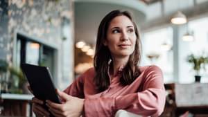 Junge Unternehmerin sitzt in einem Büro und hält nachdenklich ein Tablet in der Hand.