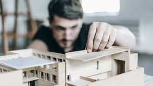 Junger Mann, der aus Holz ein Miniaturhaus baut