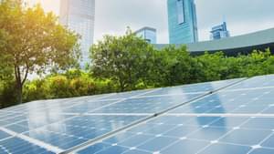 Photo of a photovoltaic system on a meadow. Trees and skyscrapers can be seen in the background.