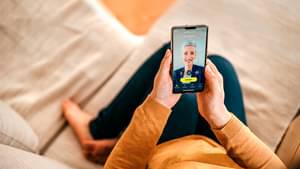 Frau sitzt bequem auf Sofa und hat Handy in den Händen