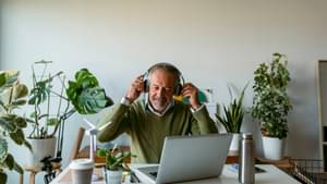 Mann mit Kopfhörern sitzt am Schreibtisch mit vielen Pflanzen im Hintergrund.
