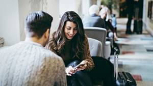 Frau am Flughafen schaut auf ihr Handy und lacht